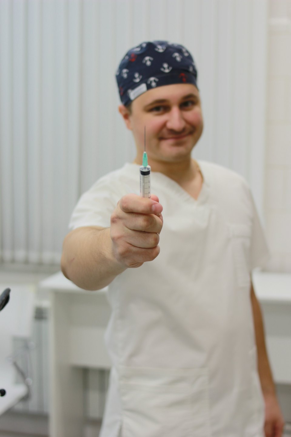Man in scrubs houdt een spuit naar de camera.