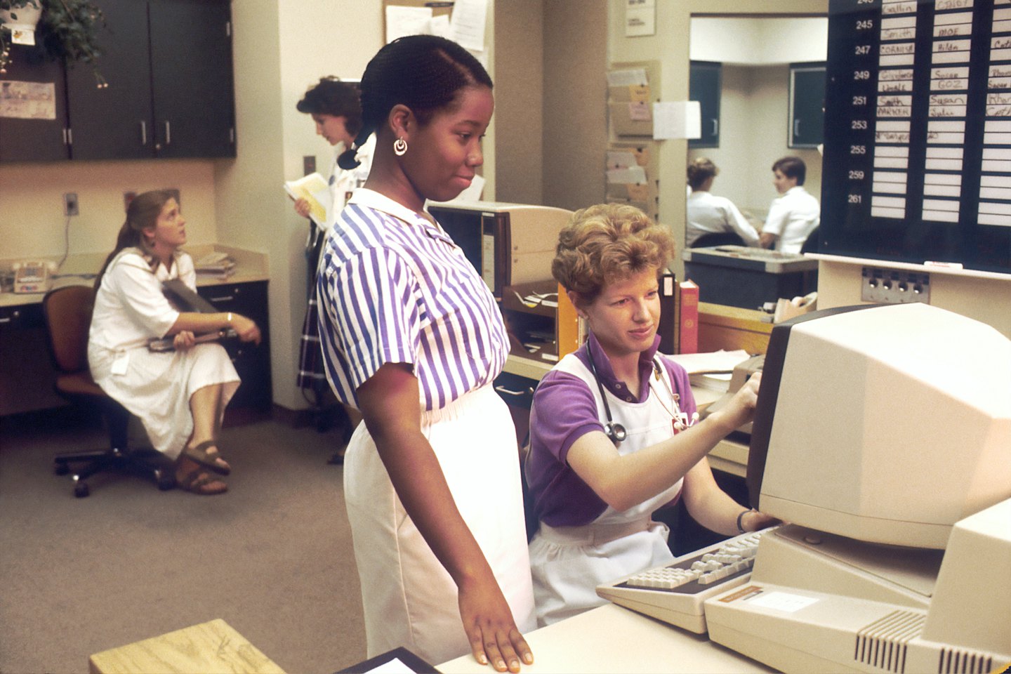 Twee zorgverleners die aan computers werken in een kantoor.